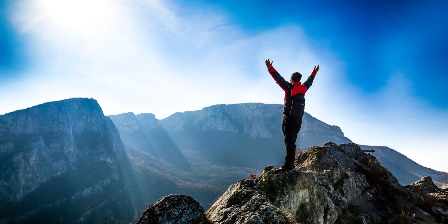 Adventurous man is standing on top of the mountain and enjoying